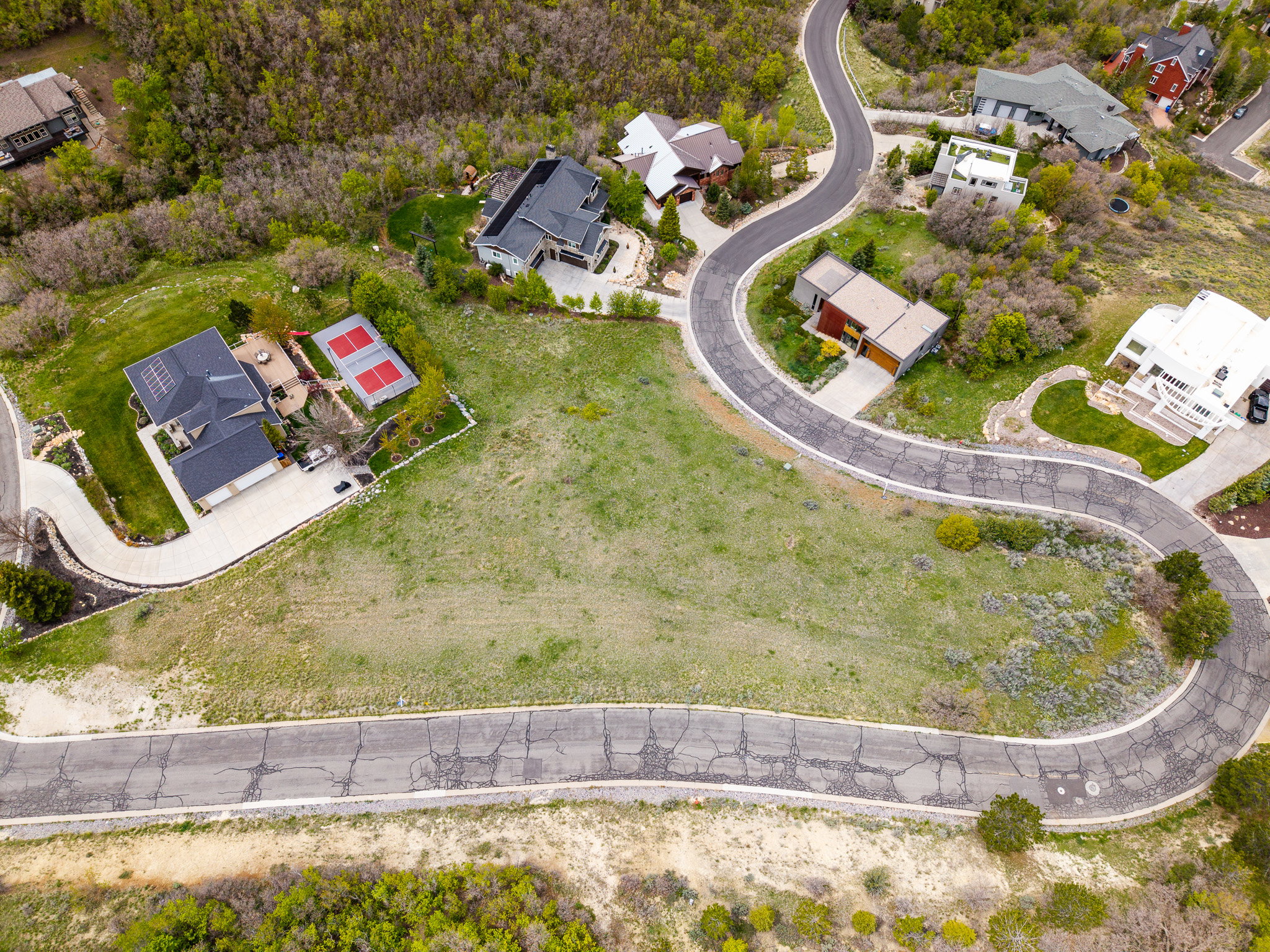Expansive land parcel featuring a curved road frontage, surrounding green spaces, and established neighboring properties