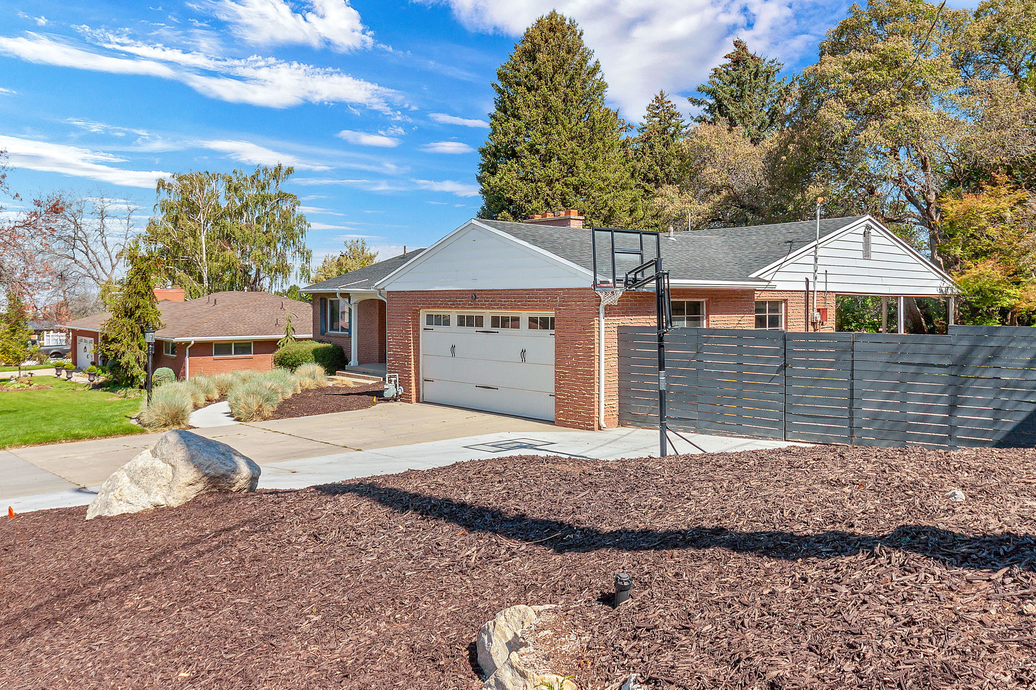 Brick exterior featuring an attached two-car garage, concrete driveway, front walkway, and mature landscaping with rock accents