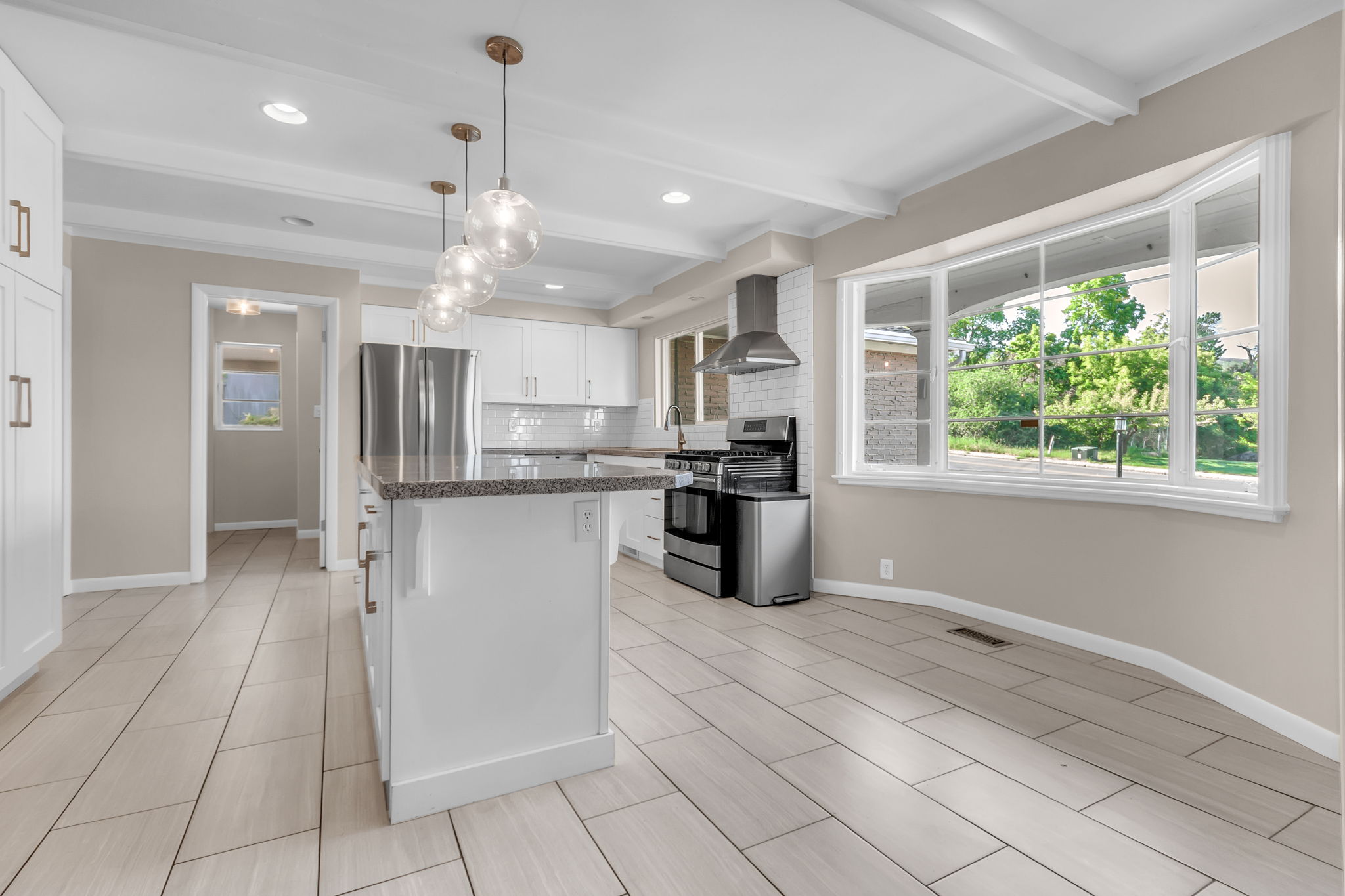 Open-concept kitchen featuring an island with a granite countertop, white shaker cabinetry, stainless steel appliances, and a subway tile backsplash