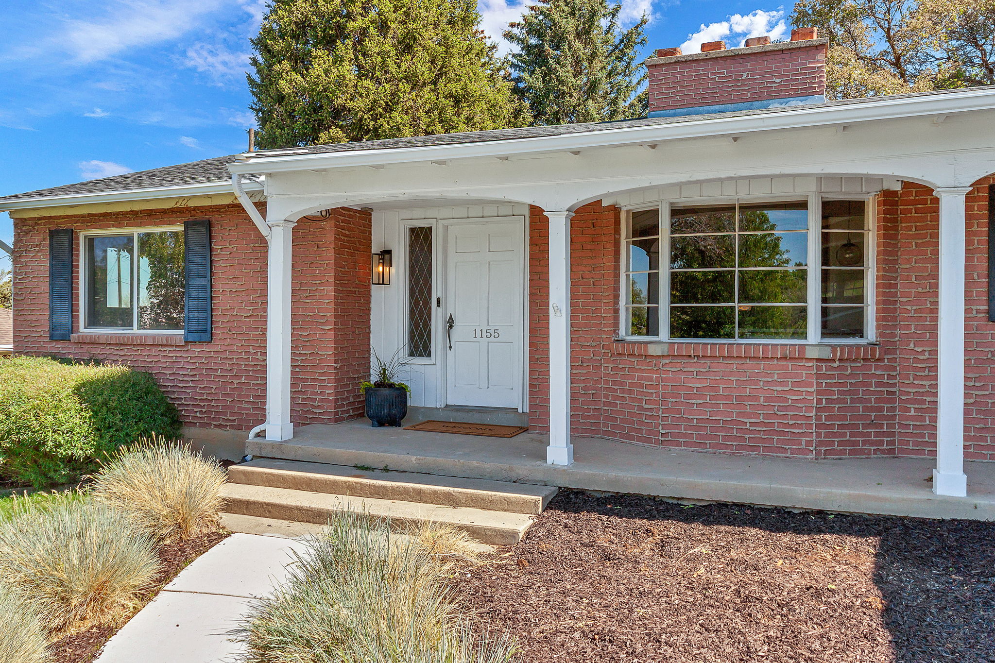 Brick exterior featuring a covered porch with white columns, a white front door with sidelight, and a bay window