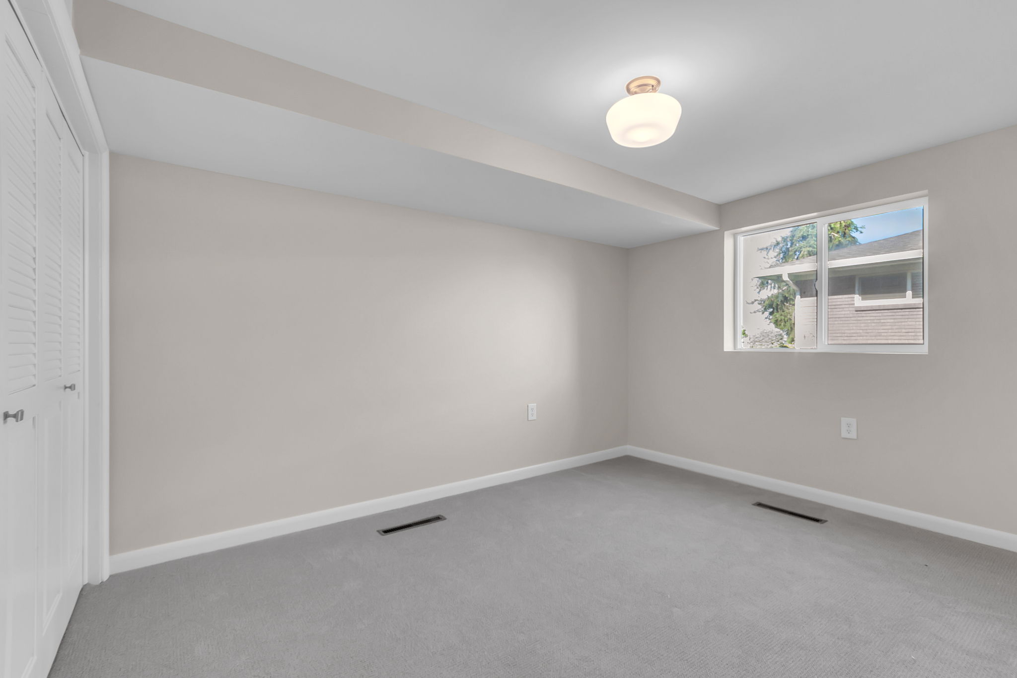 Carpeted room with a single window, a flush-mount ceiling light fixture, and louvered bifold closet doors