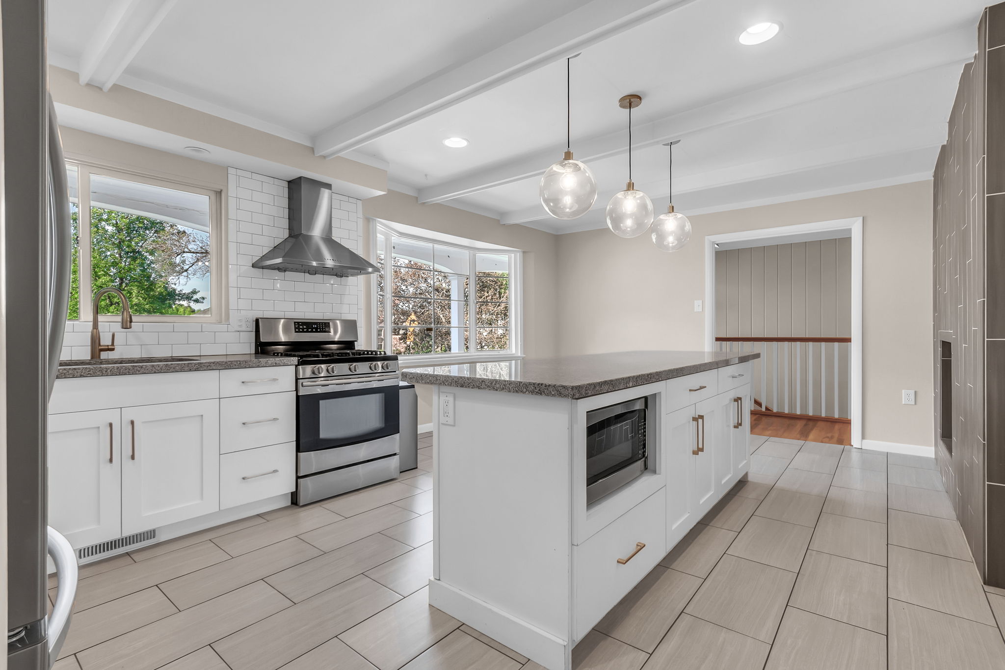 Modern kitchen featuring white cabinetry, stainless steel appliances, a center island with pendant lighting, and light tile flooring