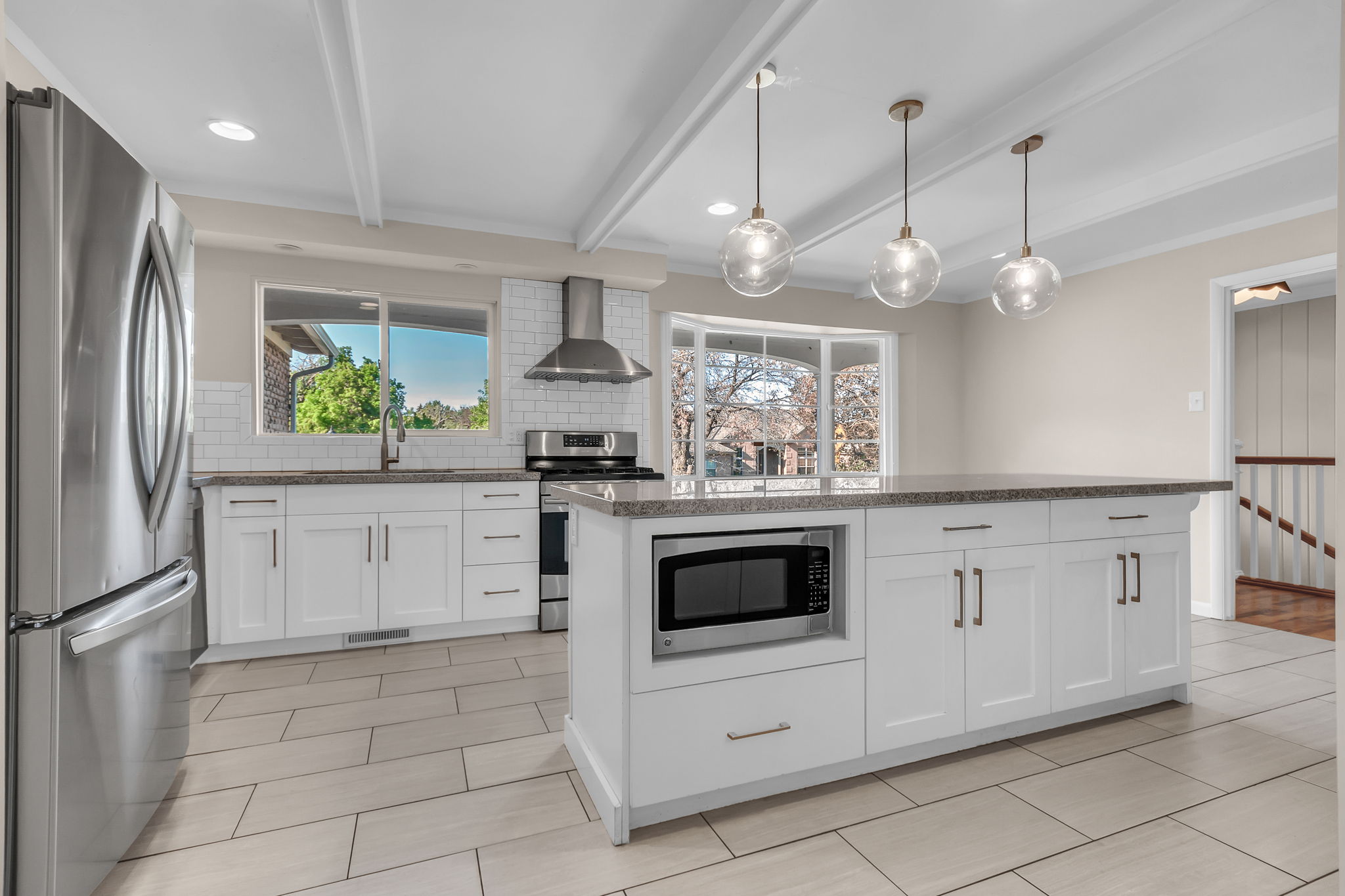 Open-concept kitchen featuring an oversized island with pendant lighting, white shaker cabinetry, stainless steel appliances, and a subway tile backsplash