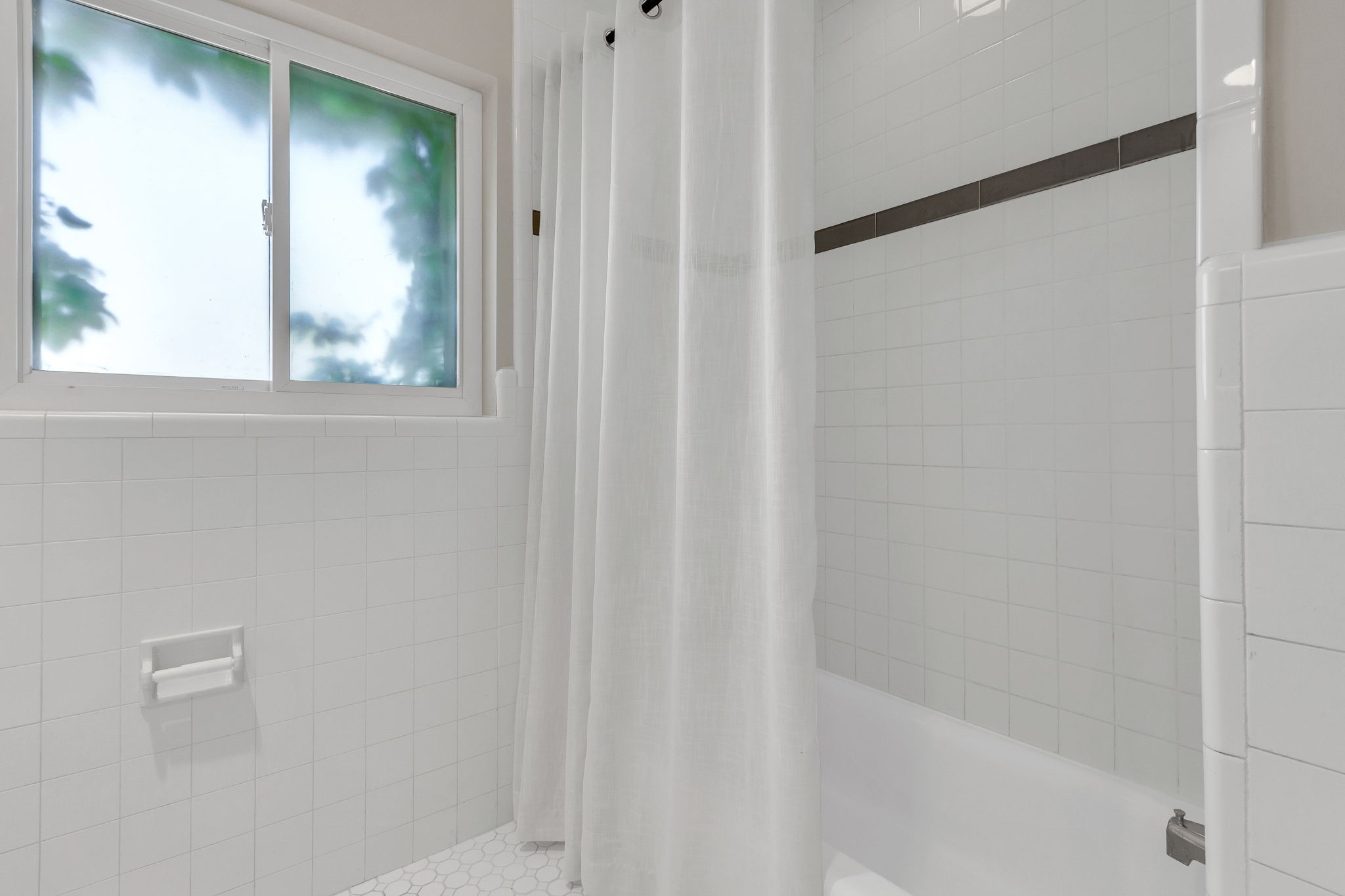 Bathroom featuring a white subway tile surround, a built-in bathtub, and a window with privacy glass
