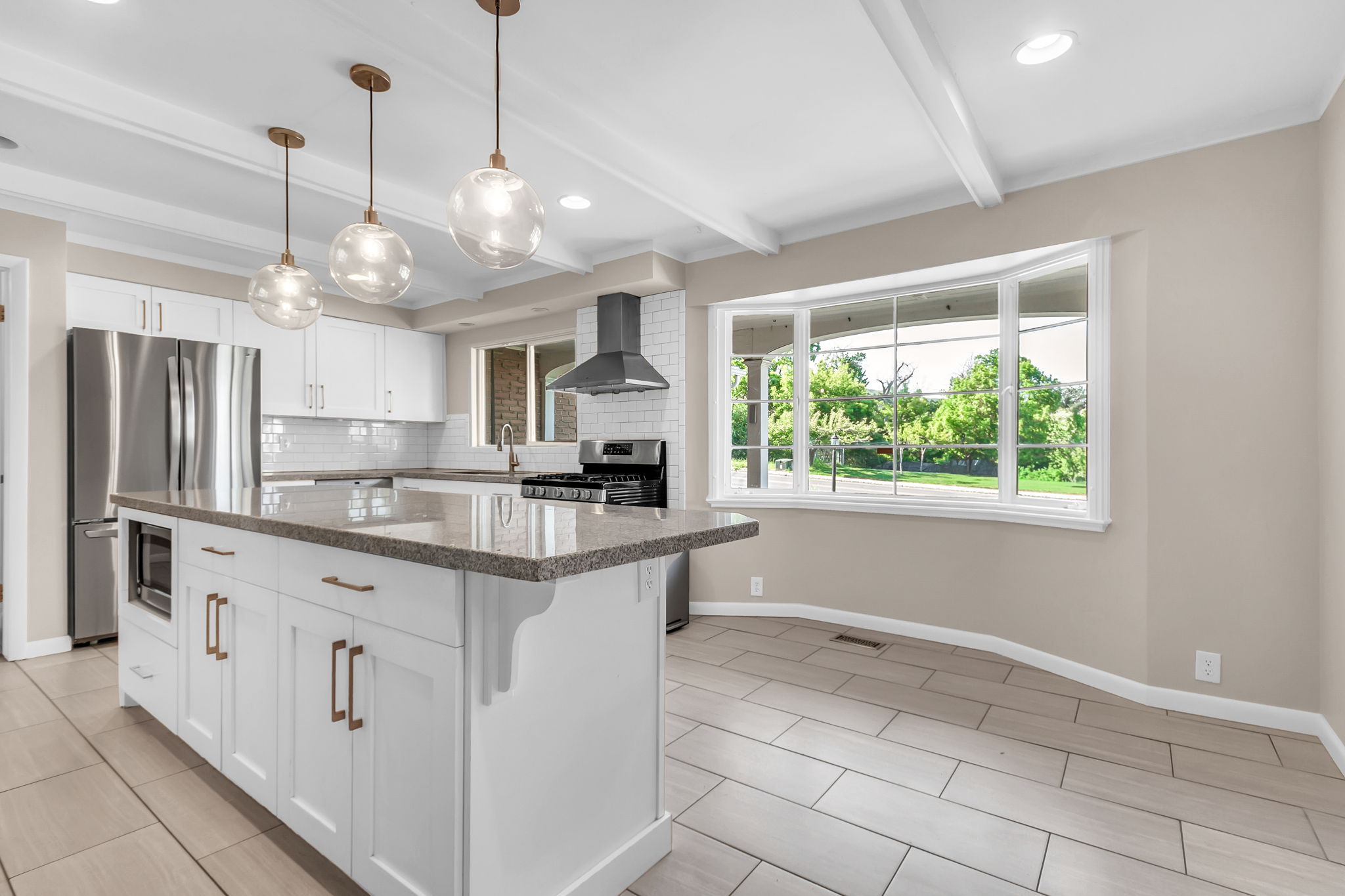 Kitchen featuring a central island with a stone countertop, white shaker-style cabinetry, stainless steel appliances, a subway tile backsplash, and a large bay window