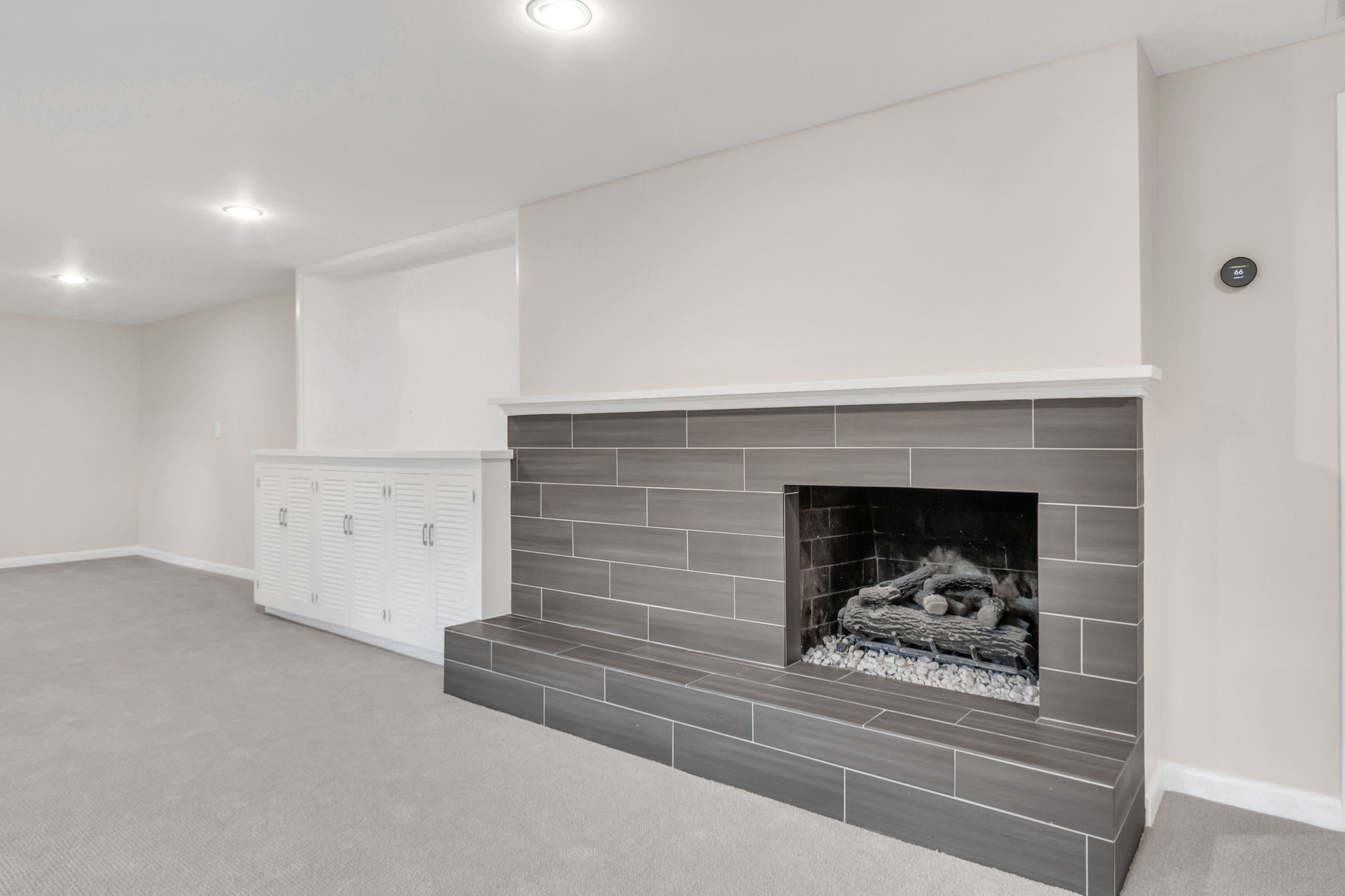 Ceramic tile fireplace with a white mantel, accompanied by built-in white louvered cabinetry, recessed lighting, and soft gray carpeting
