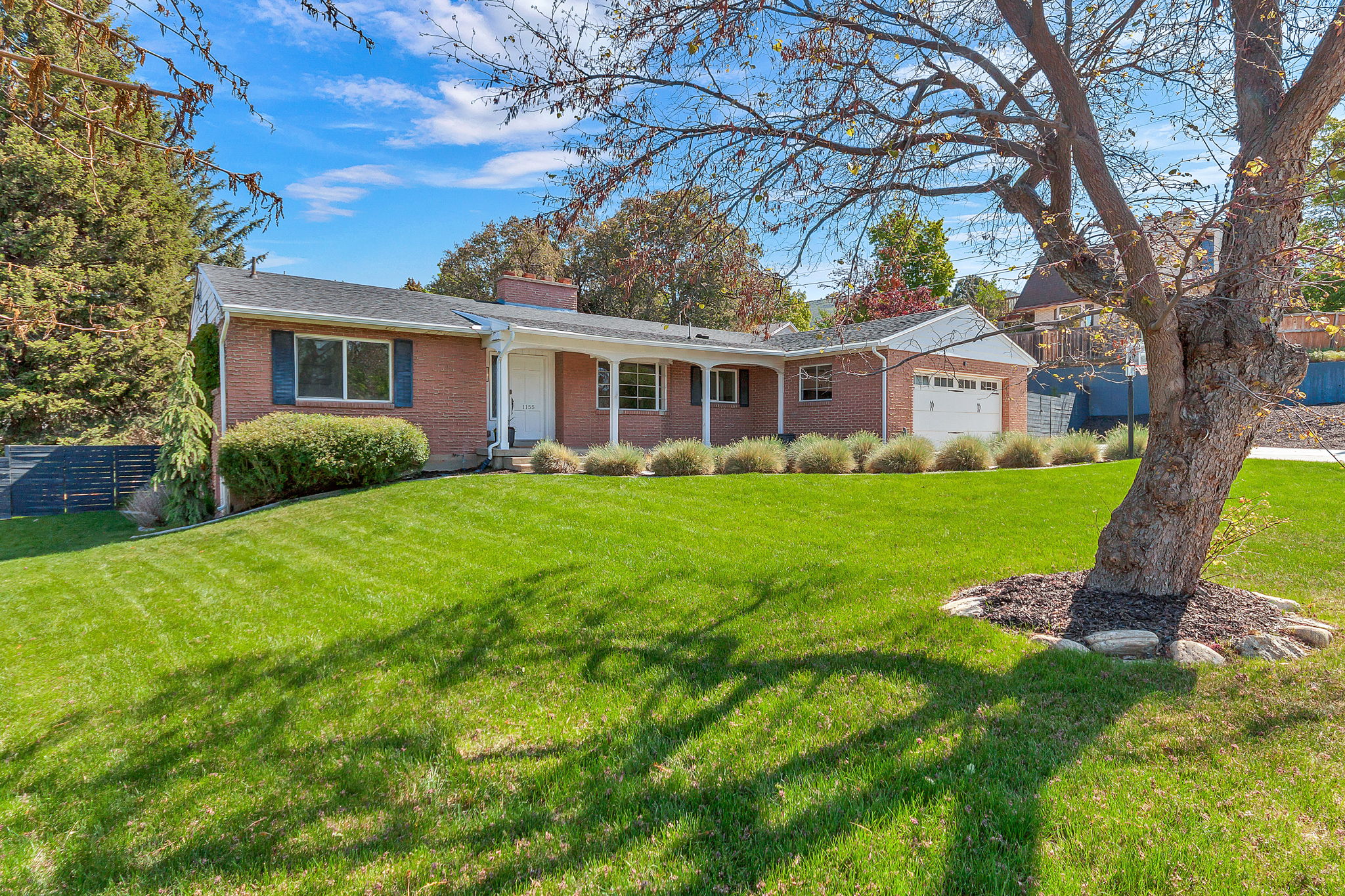 Brick exterior property featuring a covered front porch with white columns, a two-car garage with panel doors, and a large front lawn