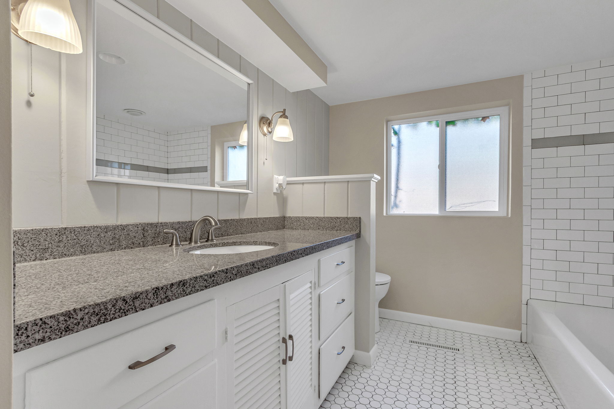 Bathroom featuring a vanity with a gray speckled countertop, white cabinetry, a built-in sink, and a framed mirror