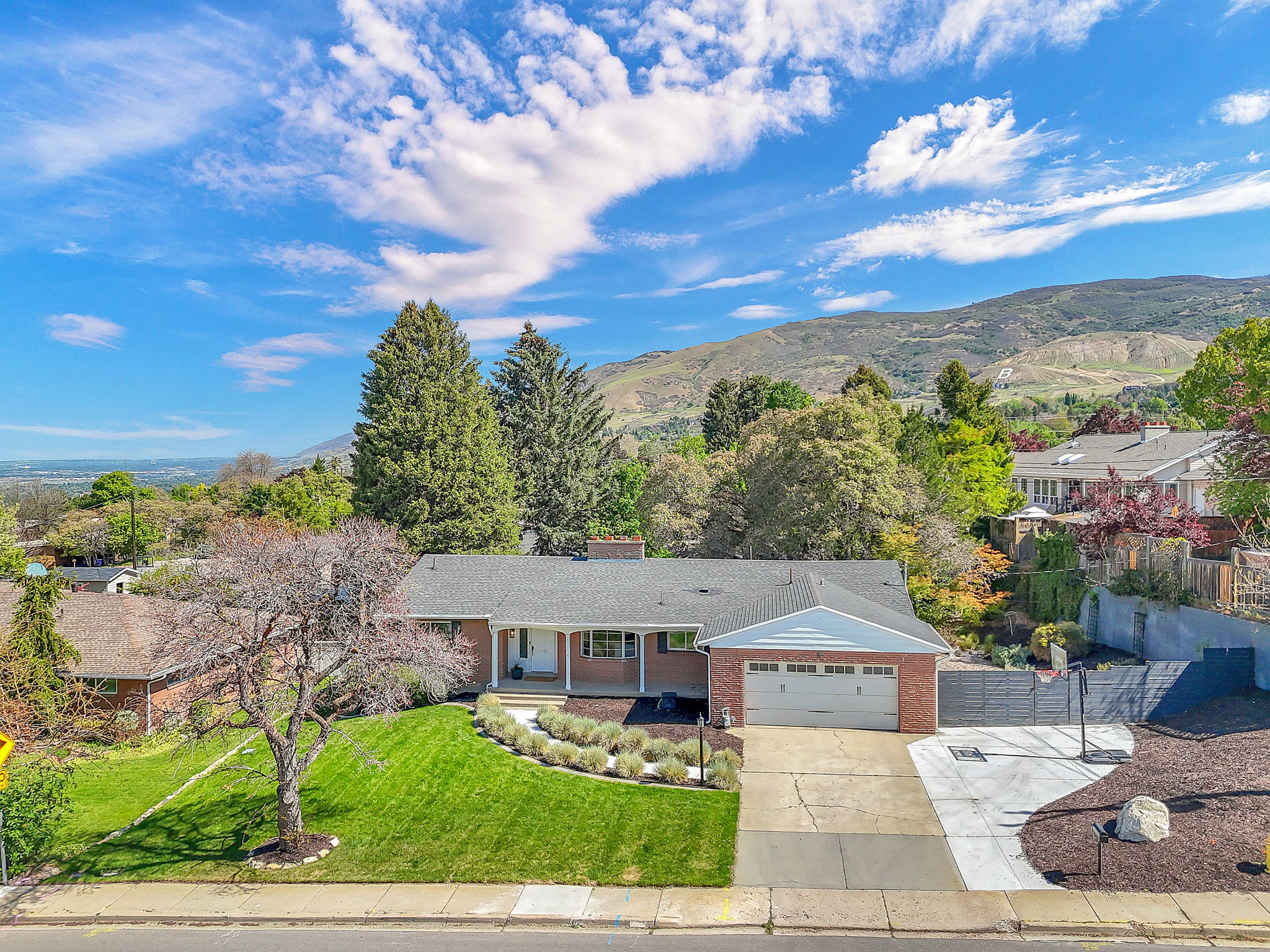 Ranch-style residence featuring a brick facade, attached two-car garage, and a lush front lawn with mature landscaping