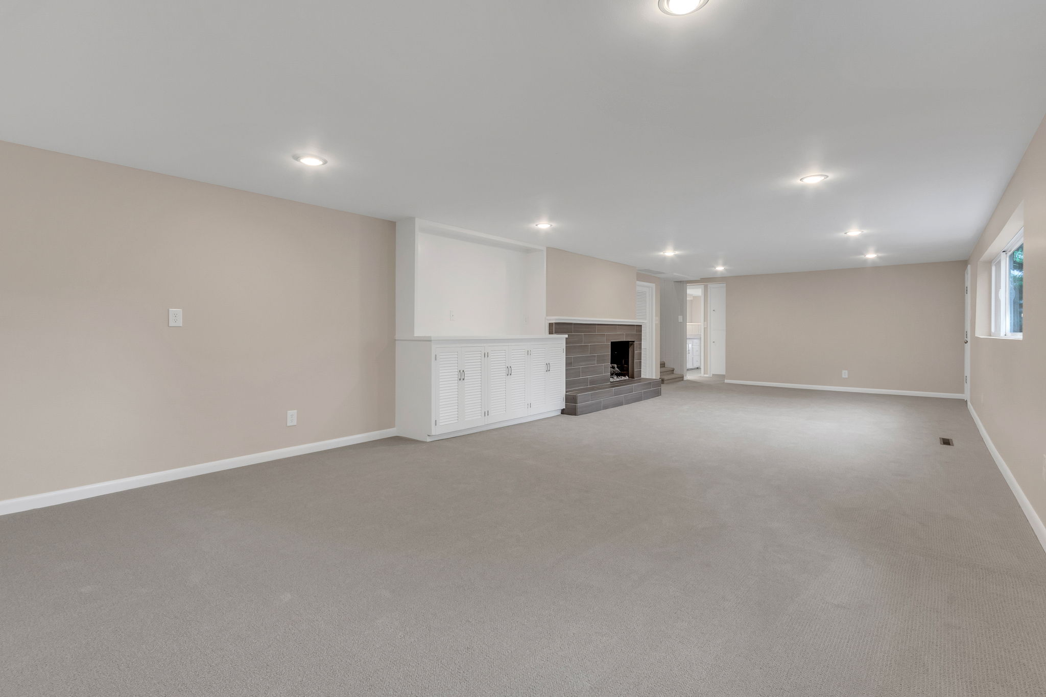 Spacious room featuring neutral carpet flooring, recessed lighting, a fireplace with a stone surround, and built-in white cabinetry