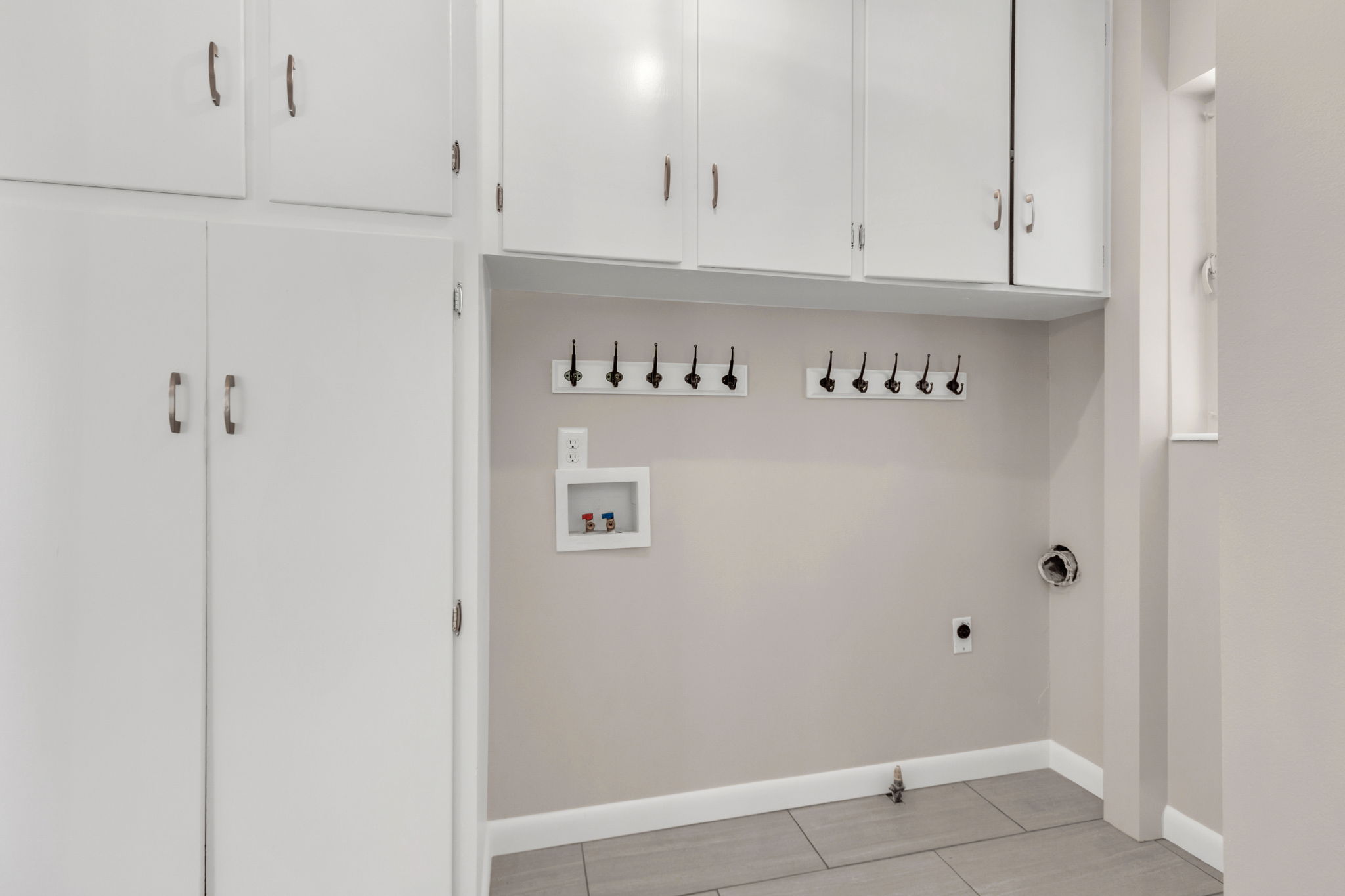 Dedicated utility space featuring ample white cabinetry, integrated wall hooks, tile flooring, and utility hookups