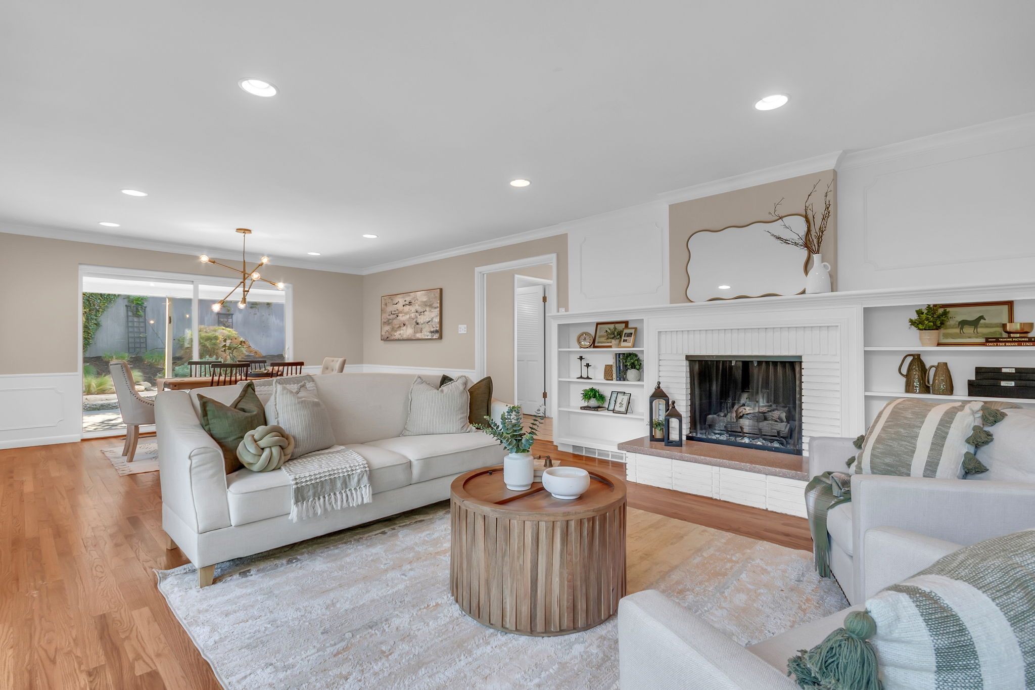 Hardwood flooring throughout featuring a white brick fireplace with built-in shelving, recessed lighting, and crown molding
