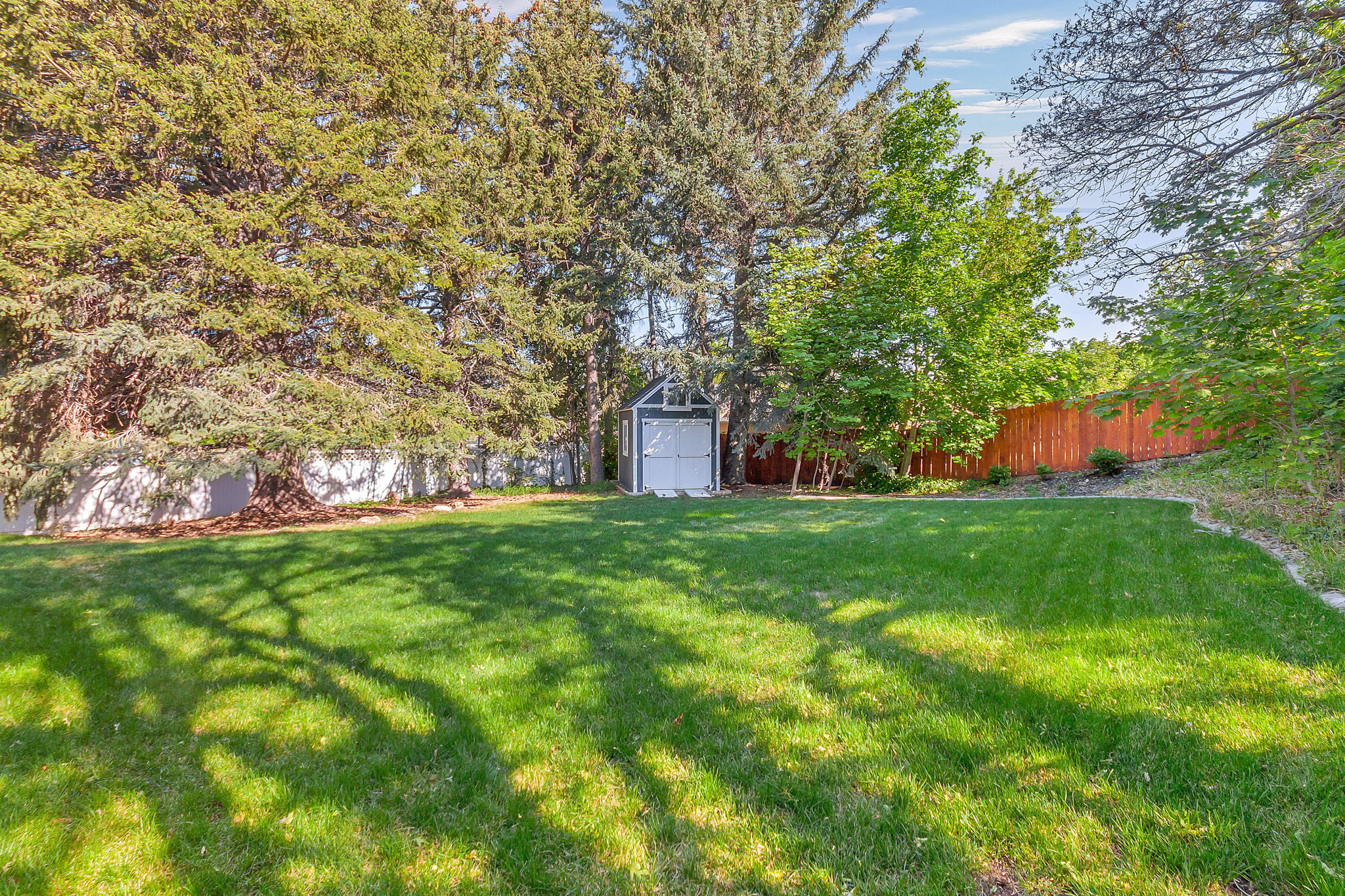 Expansive green lawn surrounded by mature trees, a white perimeter fence, and a wood fence