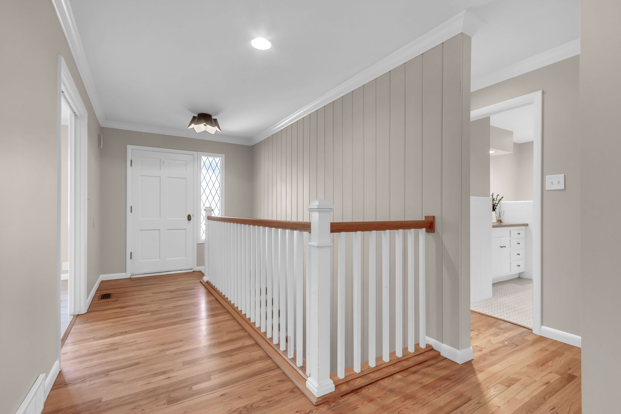 Hardwood flooring throughout the entry, spindle railing with wood-finish top rail, board and batten accent wall, decorative front door with transom window, and flush mount lighting
