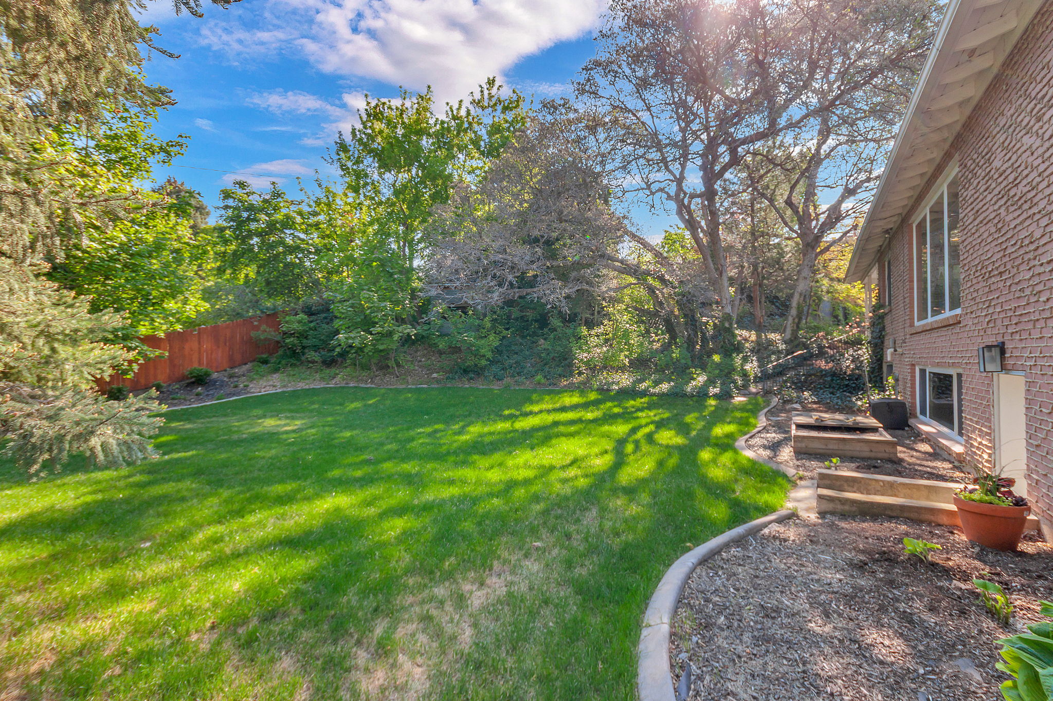 Expansive backyard featuring a manicured lawn, established perimeter landscaping, and a privacy fence