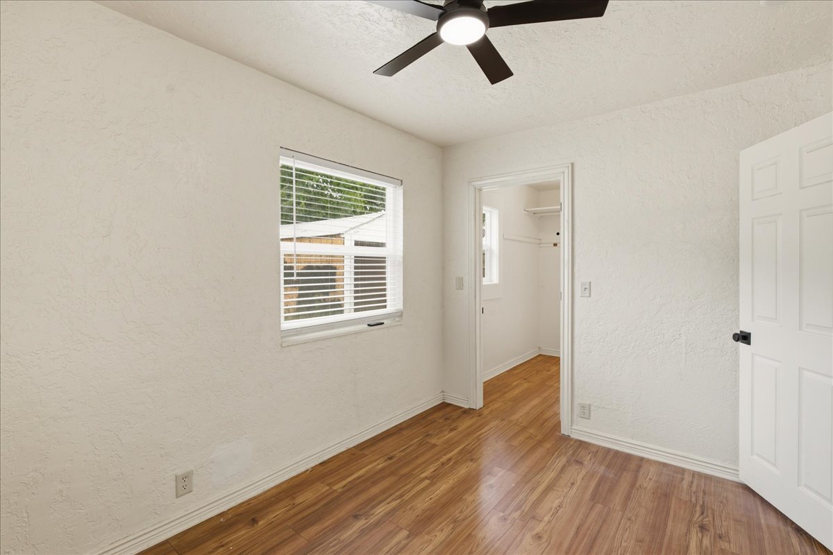 Interior room featuring wood-finish flooring, a window with horizontal blinds, and a ceiling fan
