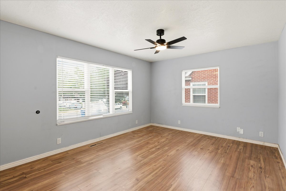 Spacious room featuring wood-finish flooring, light gray walls, white trim, and a black ceiling fan with integrated lighting