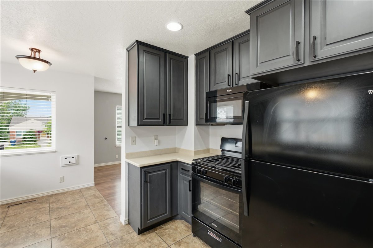 Kitchen featuring dark gray cabinetry with black hardware, light-toned countertops, a black gas range, and a black microwave
