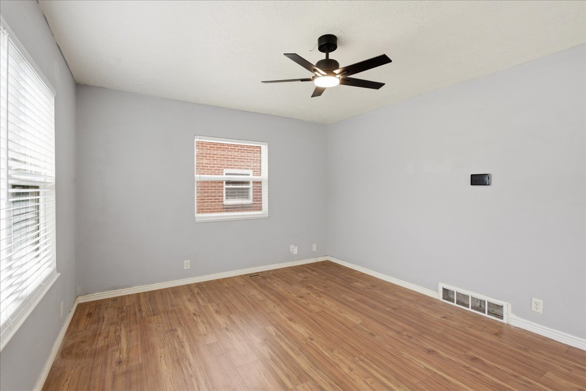 Spacious room featuring wood-finish flooring, light gray wall paint, and a modern ceiling fan with integrated lighting