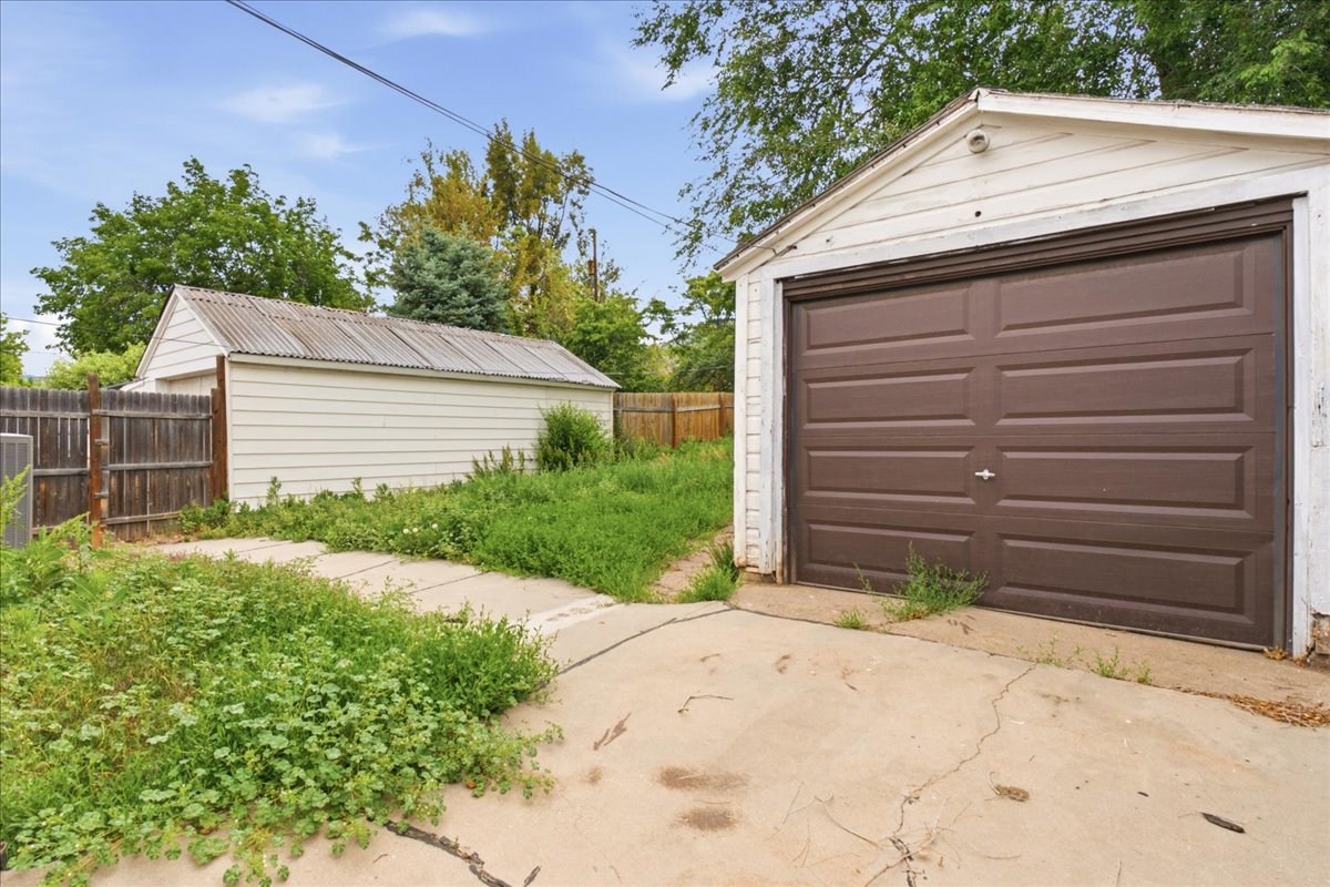 Detached garage with a brown panel door, white siding, and a gabled roof