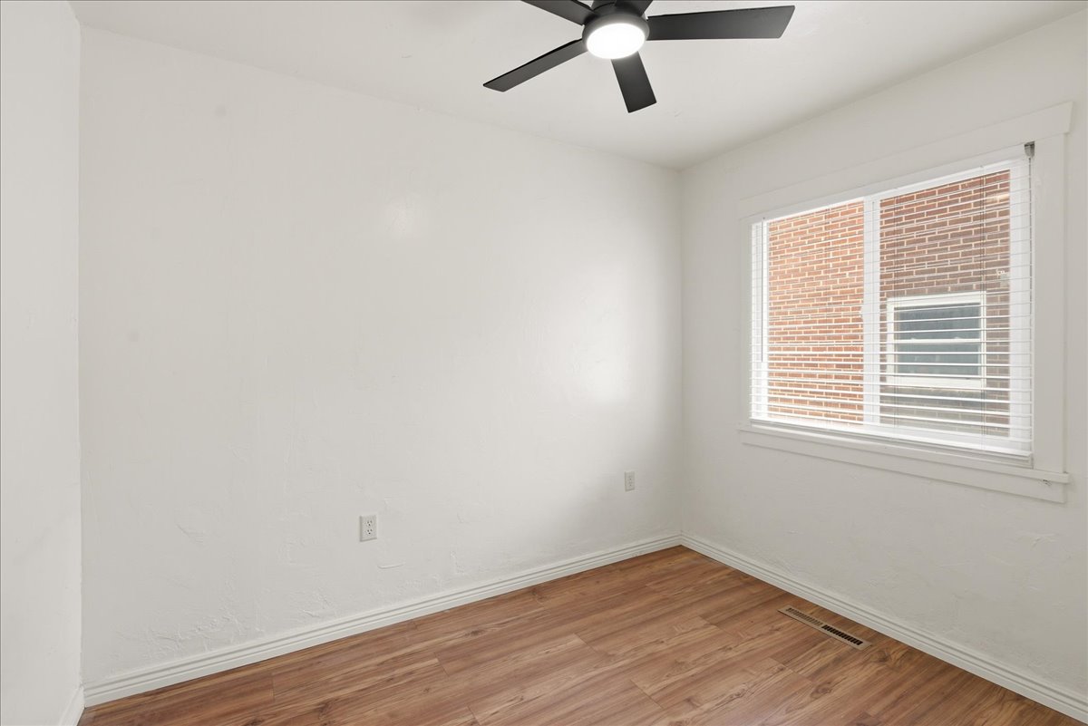 Room featuring wood-finish flooring, white walls, and a large window with white blinds