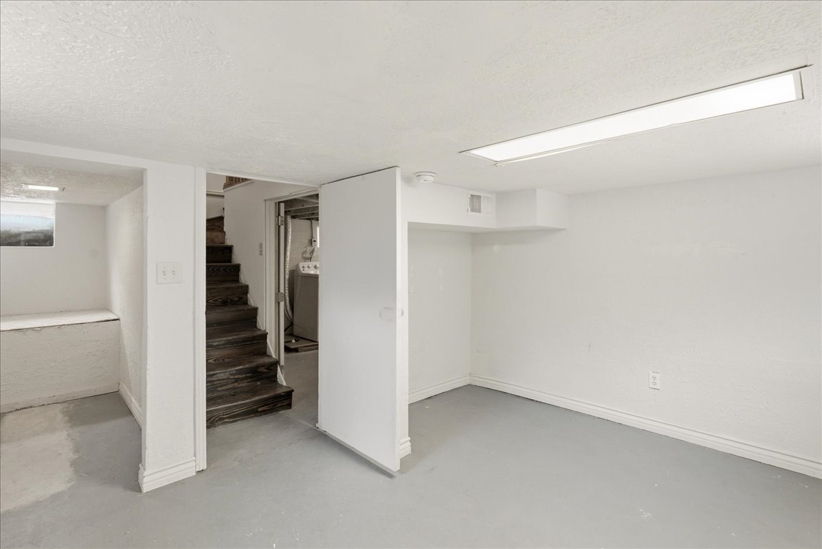 Finished basement area featuring a utility closet, painted concrete flooring, and an exposed wood staircase