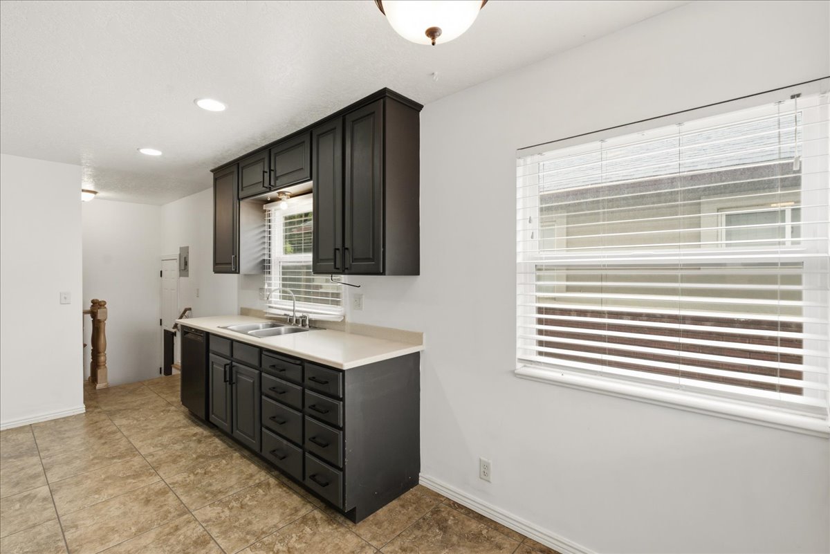 Kitchen featuring dark cabinetry, light countertops, dual basin sink with a window above, and tiled flooring
