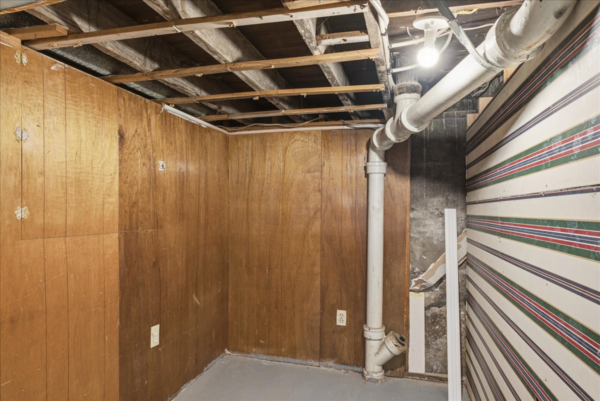 Basement area with wood paneling, exposed ceiling joists, and concrete flooring