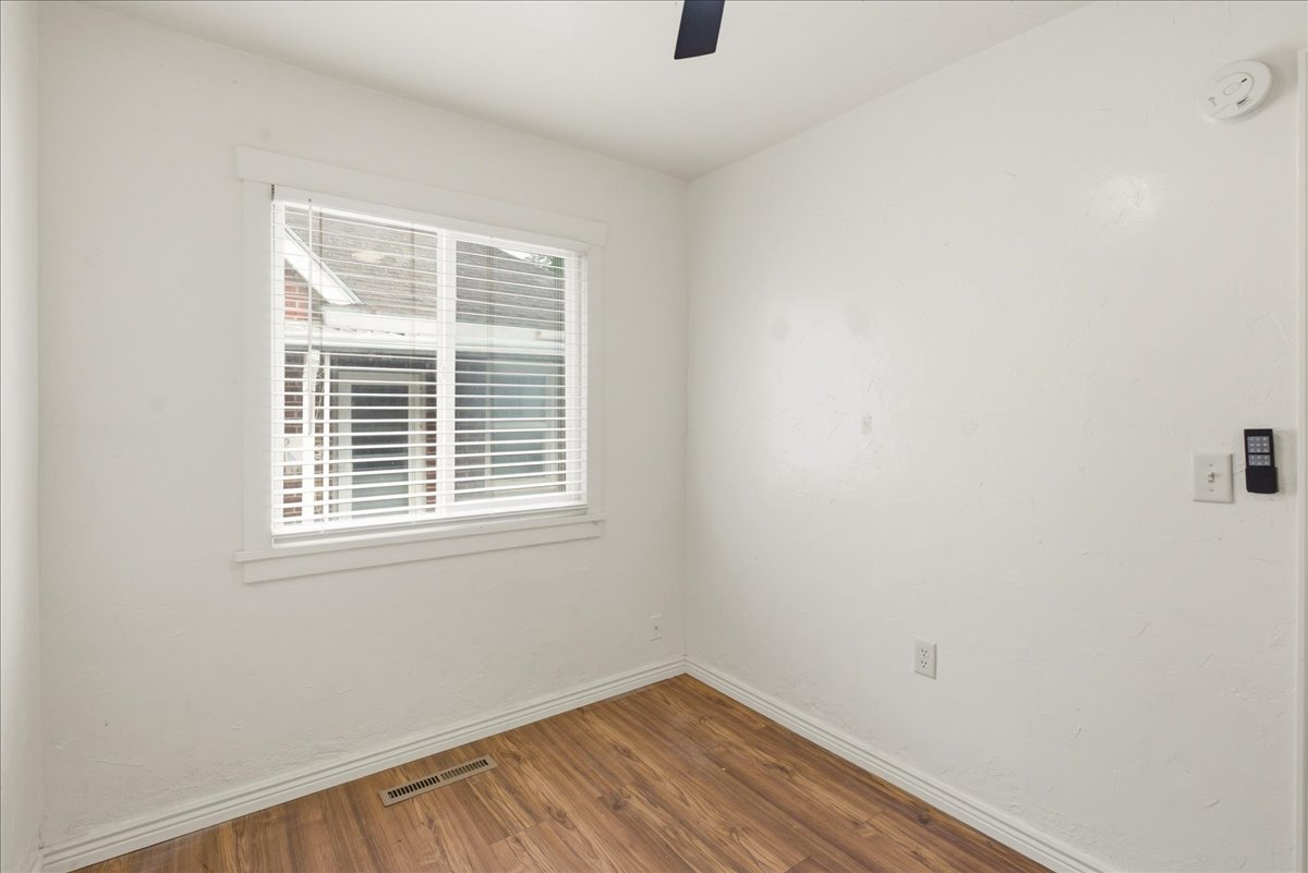 Room featuring wood-finish flooring, white walls, and a window with blinds