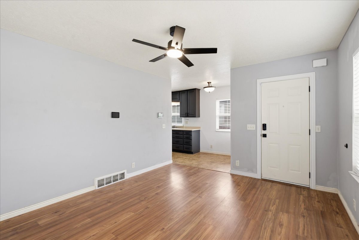 Expansive living area featuring wood-finish flooring, a contemporary ceiling fan with lighting, and a white paneled entry door