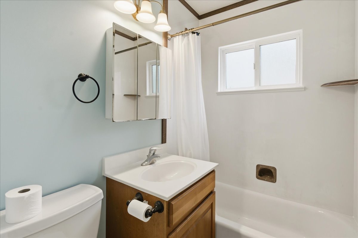 Bathroom featuring a single vanity with a white countertop and wood-finish cabinetry, a mirrored medicine cabinet, and a window above the bathtub