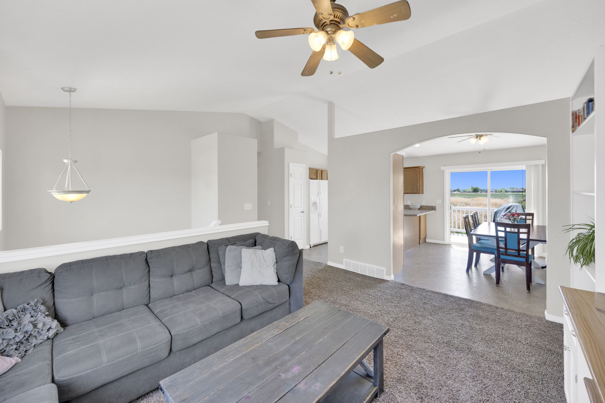Living area featuring a textured carpet floor, vaulted ceiling, and a ceiling fan