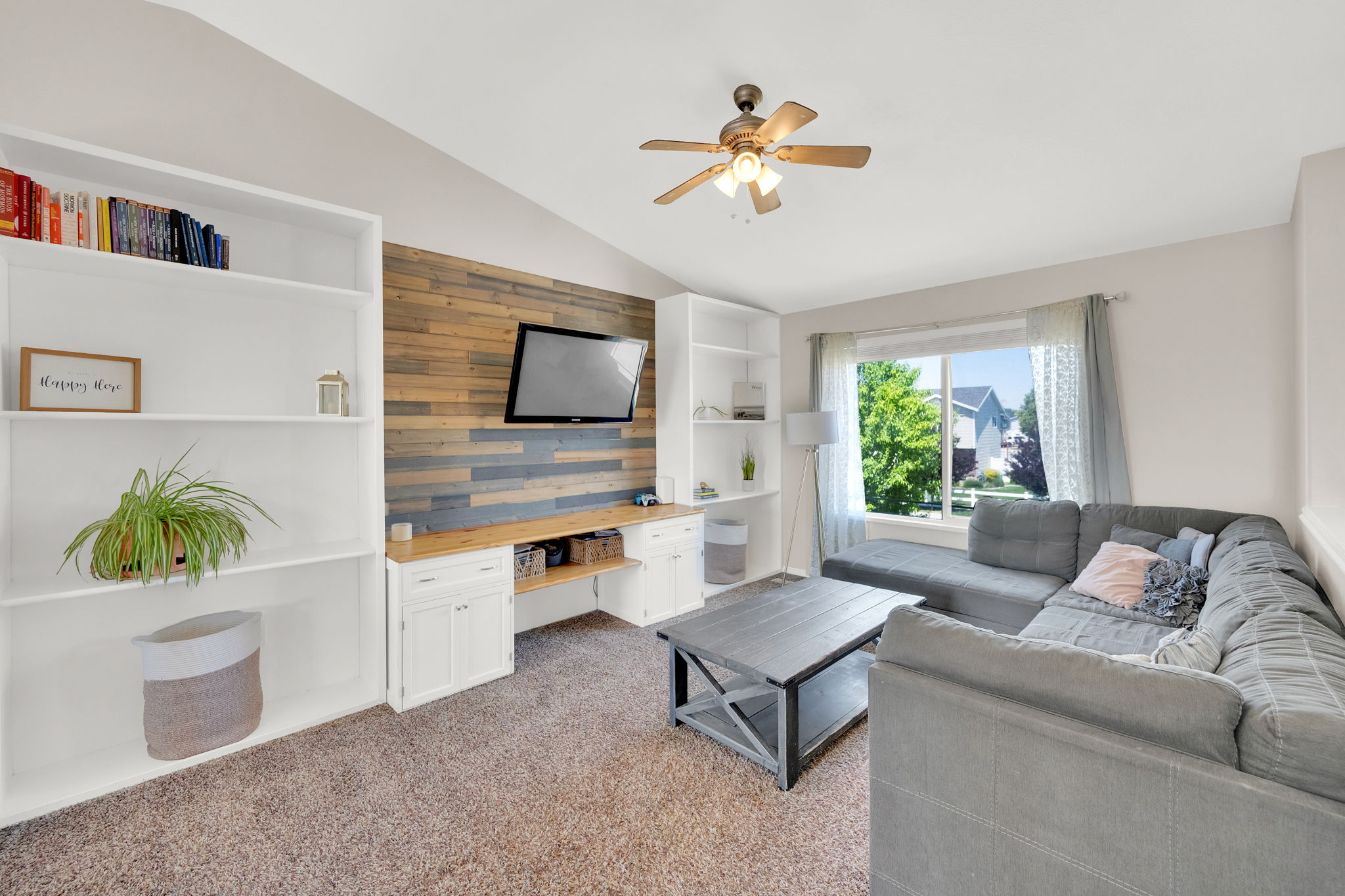 Living area featuring a vaulted ceiling with a ceiling fan, a large window, and carpet flooring