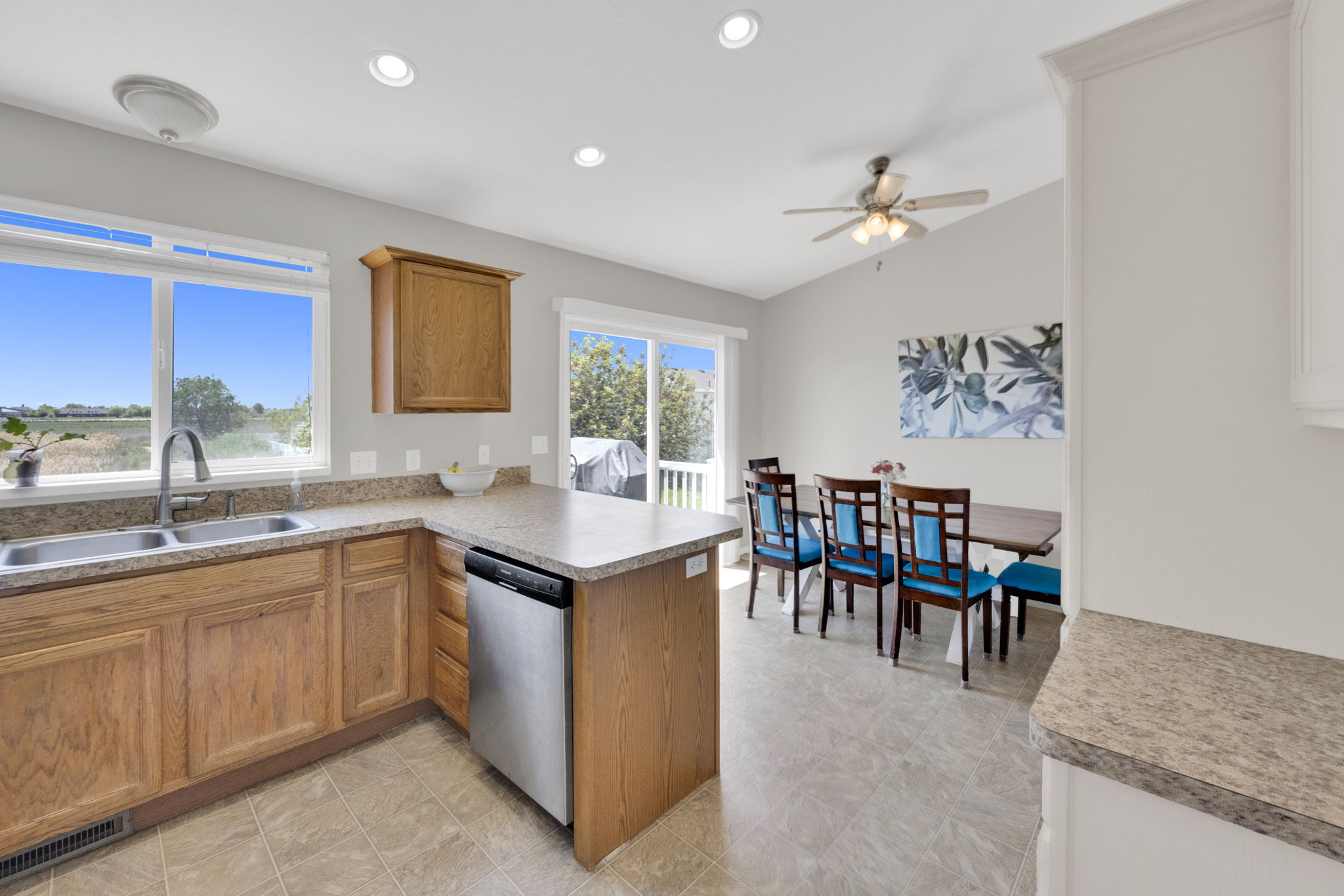 Kitchen and dining area featuring a double basin stainless steel sink, wood cabinetry, stainless steel dishwasher, and a vaulted ceiling