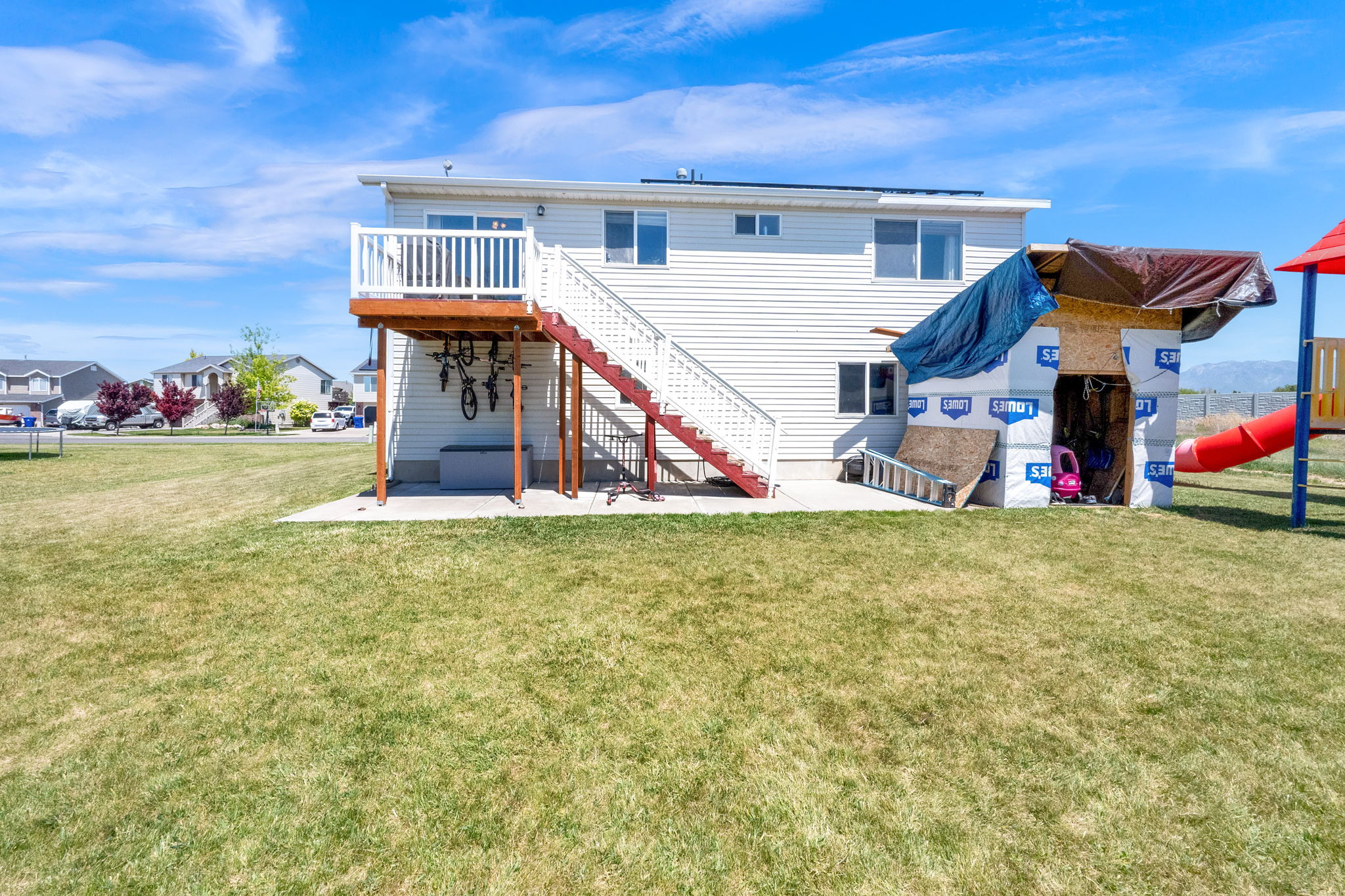Rear exterior featuring white vinyl siding, a wood deck with white railings, and an expansive lawn