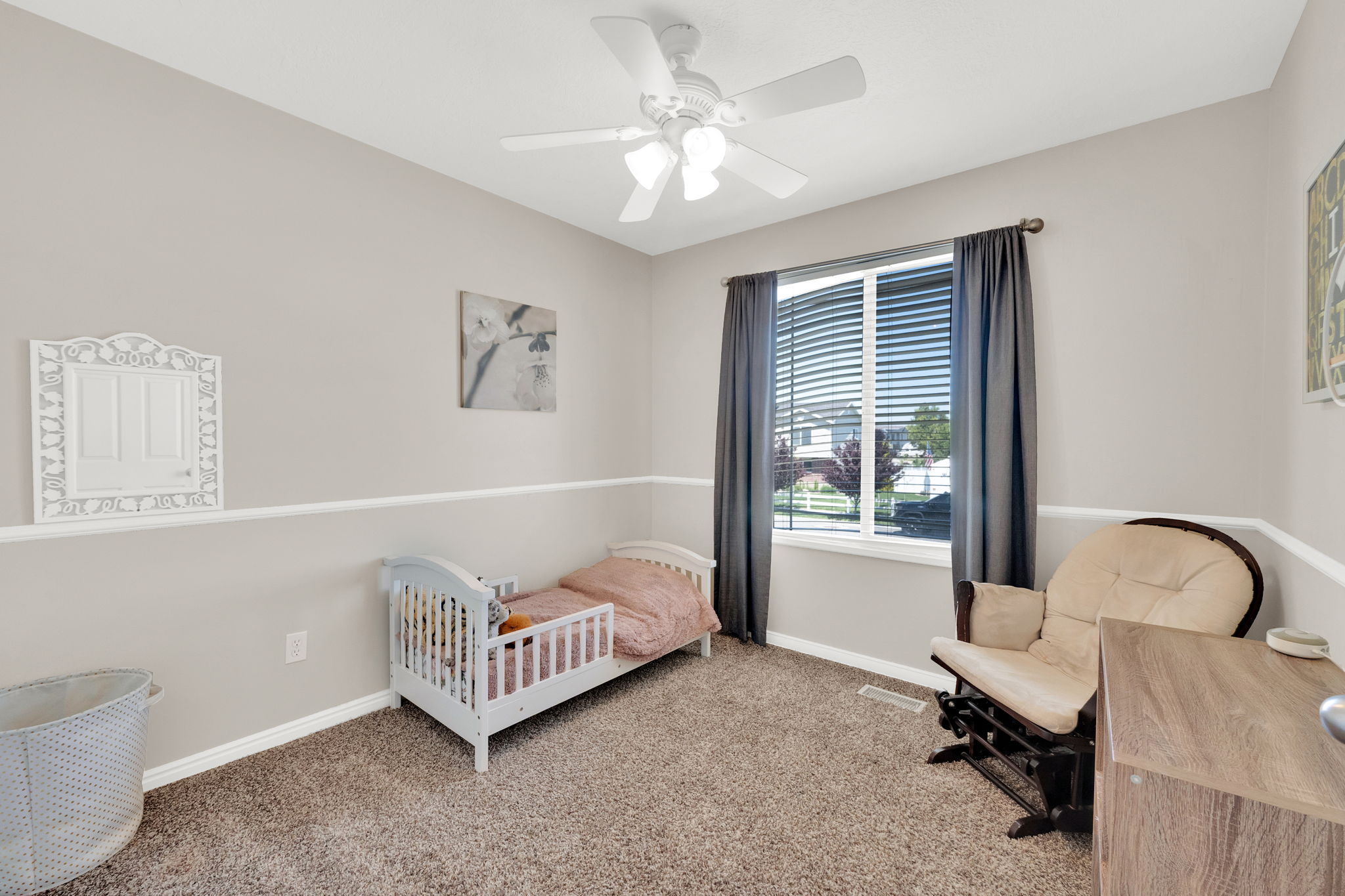 Carpeted room featuring a ceiling fan with integrated lighting, a window with blinds and drapes, and neutral two-tone wall paint with a chair rail