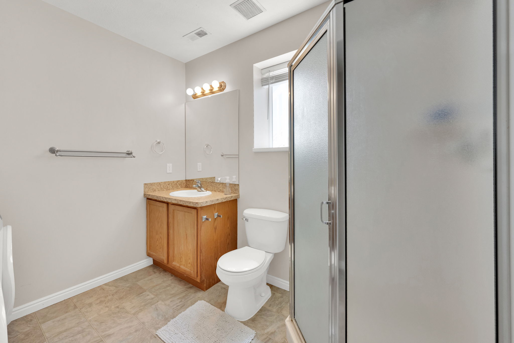 Bathroom featuring a glass-enclosed shower, single vanity with wood cabinetry, and a window for natural light