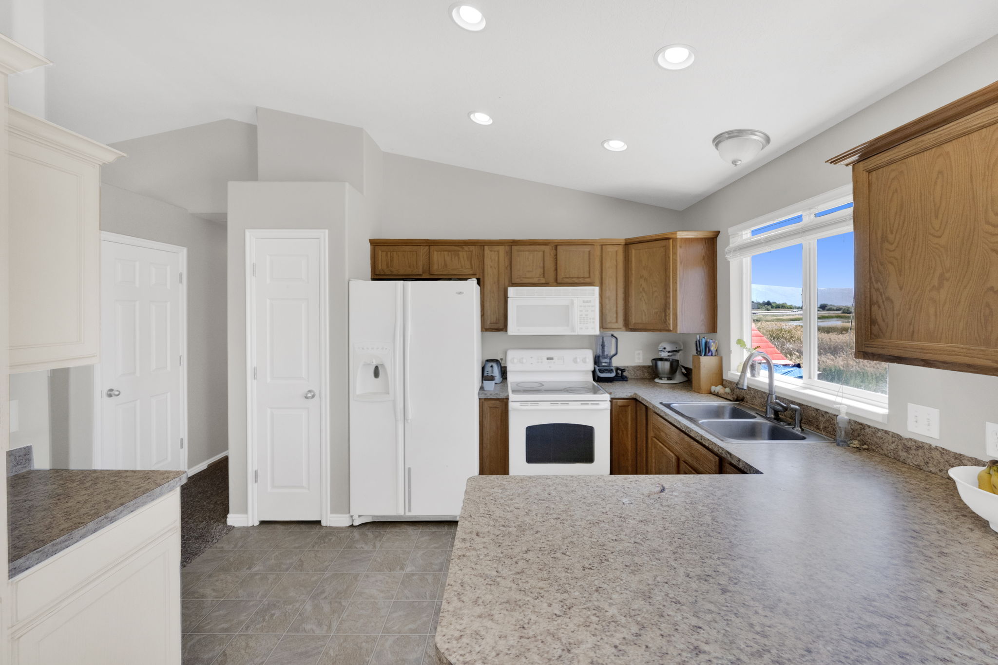Spacious kitchen featuring warm wood cabinetry, neutral countertops, and white appliances