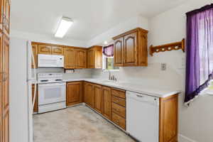 U-shaped kitchen featuring wood cabinetry, white countertops, a white oven/range, a built-in microwave, and a white dishwasher