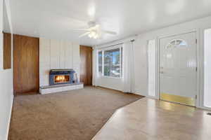 Living area featuring a brick fireplace with an insert, wood paneling, a ceiling fan, and a front entry door with a sidelight