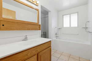 Bathroom featuring a vanity with a white countertop and integral sink, a large wood-framed mirror, and a built-in bathtub with an overhead shower fixture
