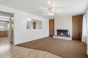 Living space featuring a brick fireplace with a black insert, wood-paneled accents, and a ceiling fan