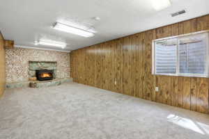 Spacious room featuring wood paneling, light gray carpeting, and a stone fireplace with a wood-burning insert