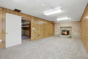 Spacious room featuring a stone fireplace with hearth, wood paneling, textured accent wall, light-toned carpeting, and recessed lighting