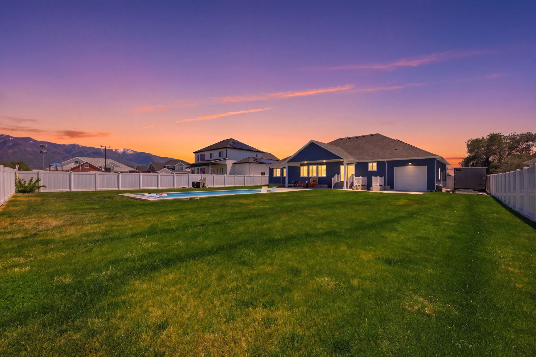 Expansive backyard featuring a manicured lawn, an in-ground swimming pool, and a white picket fence enclosing the perimeter