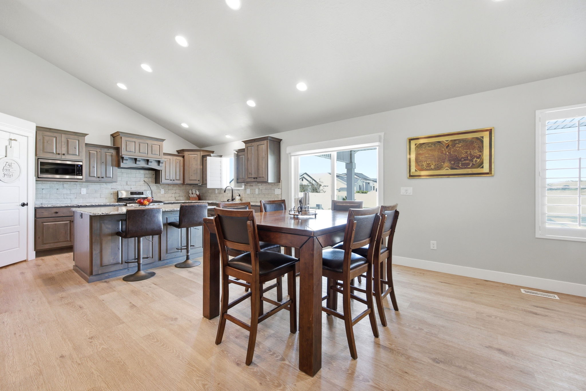 Vaulted ceiling kitchen featuring wood-finish flooring, shaker-style cabinetry, a kitchen island with seating, a tile backsplash, and stainless steel appliances