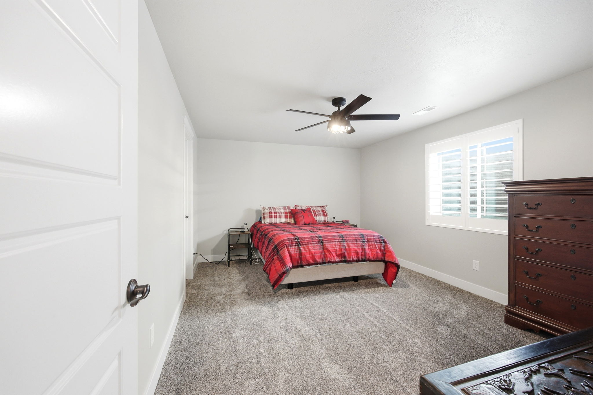 Carpeted room featuring light gray walls, a window with plantation shutters, white baseboards, and a ceiling fan with integrated lighting
