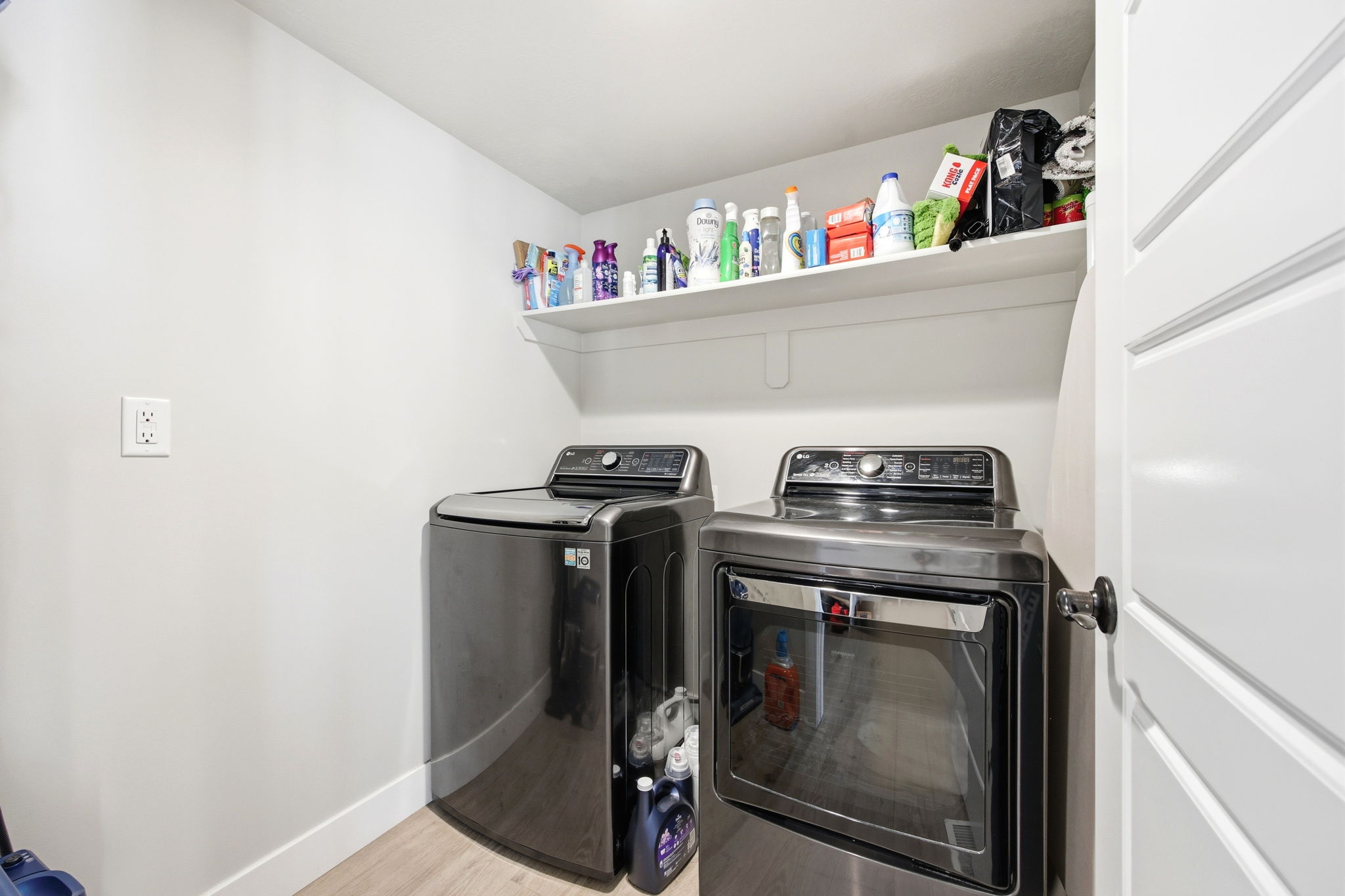 Dedicated laundry area featuring a wall-mounted shelf, light wood-finish flooring, and a white interior door with a black handle