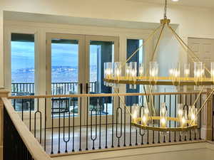 Two-tiered gold-finish chandelier with glass shades, wood-finish flooring, black wrought iron railing, and French doors opening to an exterior balcony
