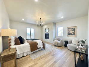 Spacious room featuring wood-finish flooring, a contemporary black metal chandelier, a built-in fireplace with a circular mirror above, and recessed lighting